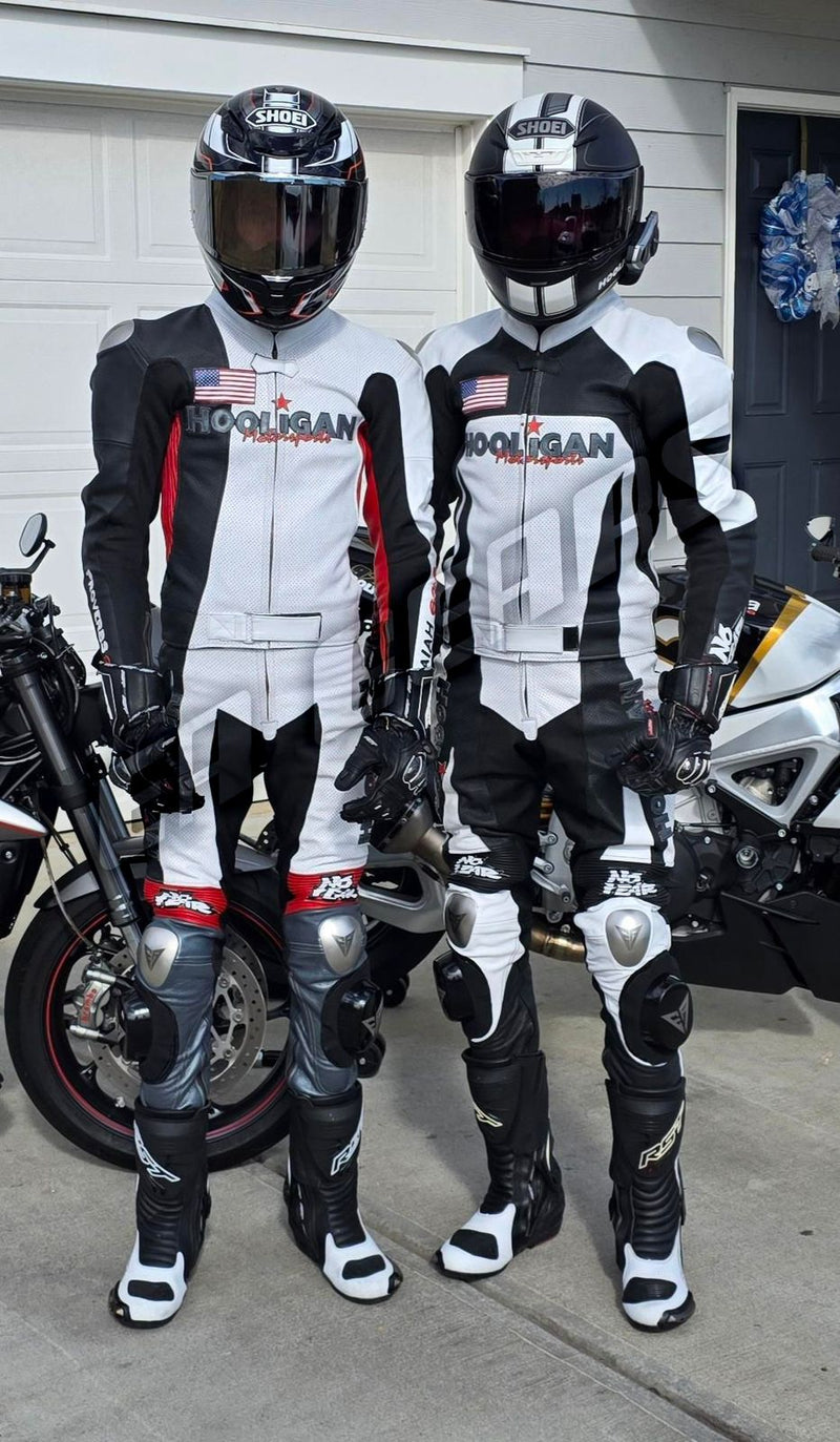 Two people in motorcycle gear standing next to motorcycles, wearing helmets and suits with visible branding.