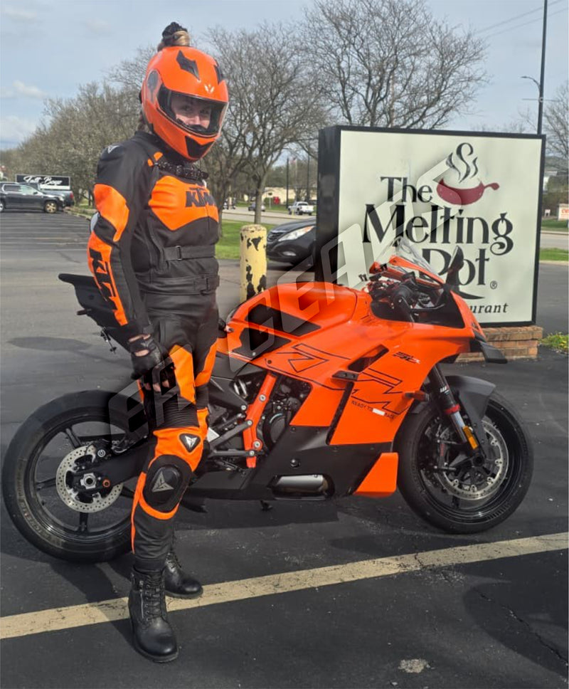 Person in orange and black motorcycle gear standing next to an orange motorcycle in a parking lot with 'The Melting Pot' restaurant sign.